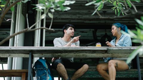 A couple enjoys drinks and conversation at an outdoor café table surrounded by greenery.