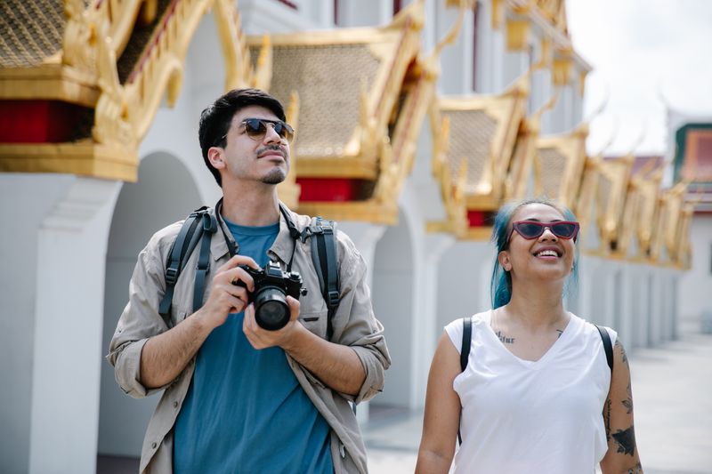 A couple explores a city's ornate architecture, capturing memories with a camera.