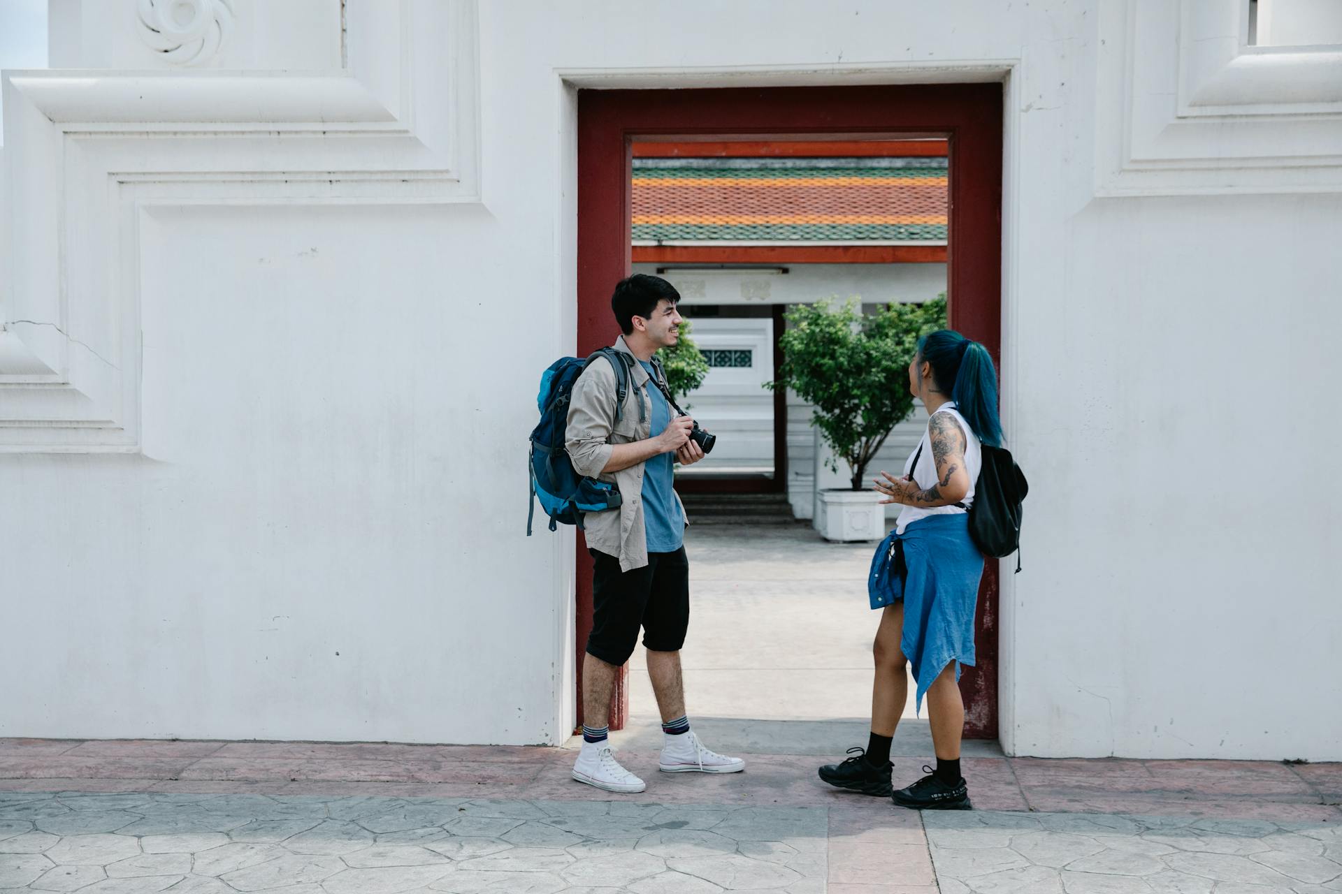 Two young travelers with backpacks share a moment at a cultural landmark, blending contemporary style with tradition.