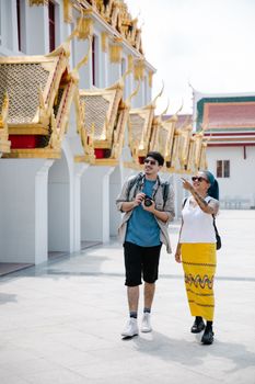 Two tourists exploring a traditional Thai temple with intricate gold architectural details.