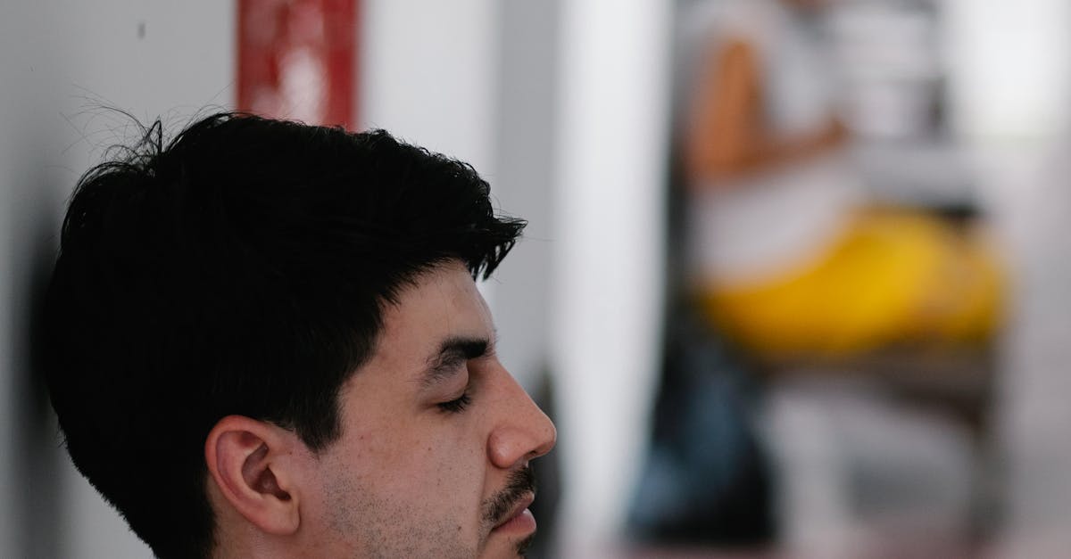 Side view of a man meditating indoors, focusing with eyes closed in an urban environment.
