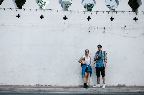 Free A happy couple in casual wear posing against a historic white wall during their travels. Stock Photo