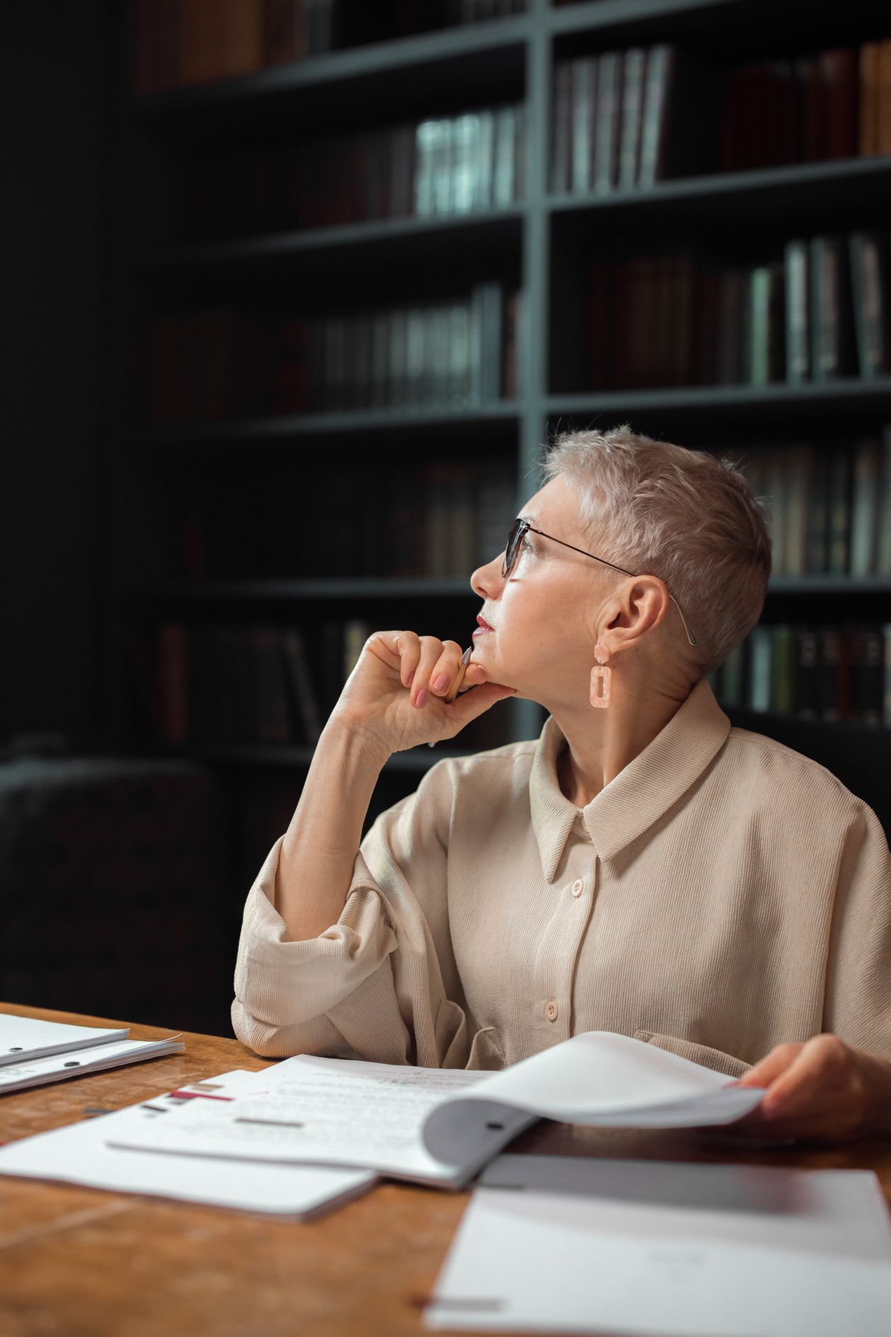 Woman in a beige blouse sitting at a wooden desk in a library.