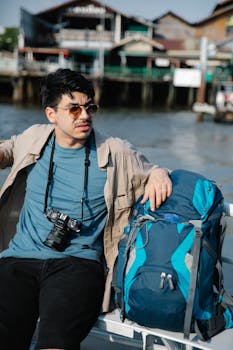 Man with camera and backpack relaxing by the waterfront, enjoying the view on a sunny day.