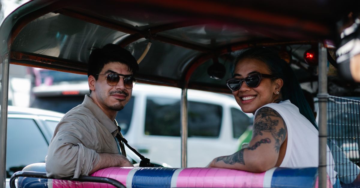 Smiling couple enjoying a scenic ride in an auto rickshaw on a sunny day.