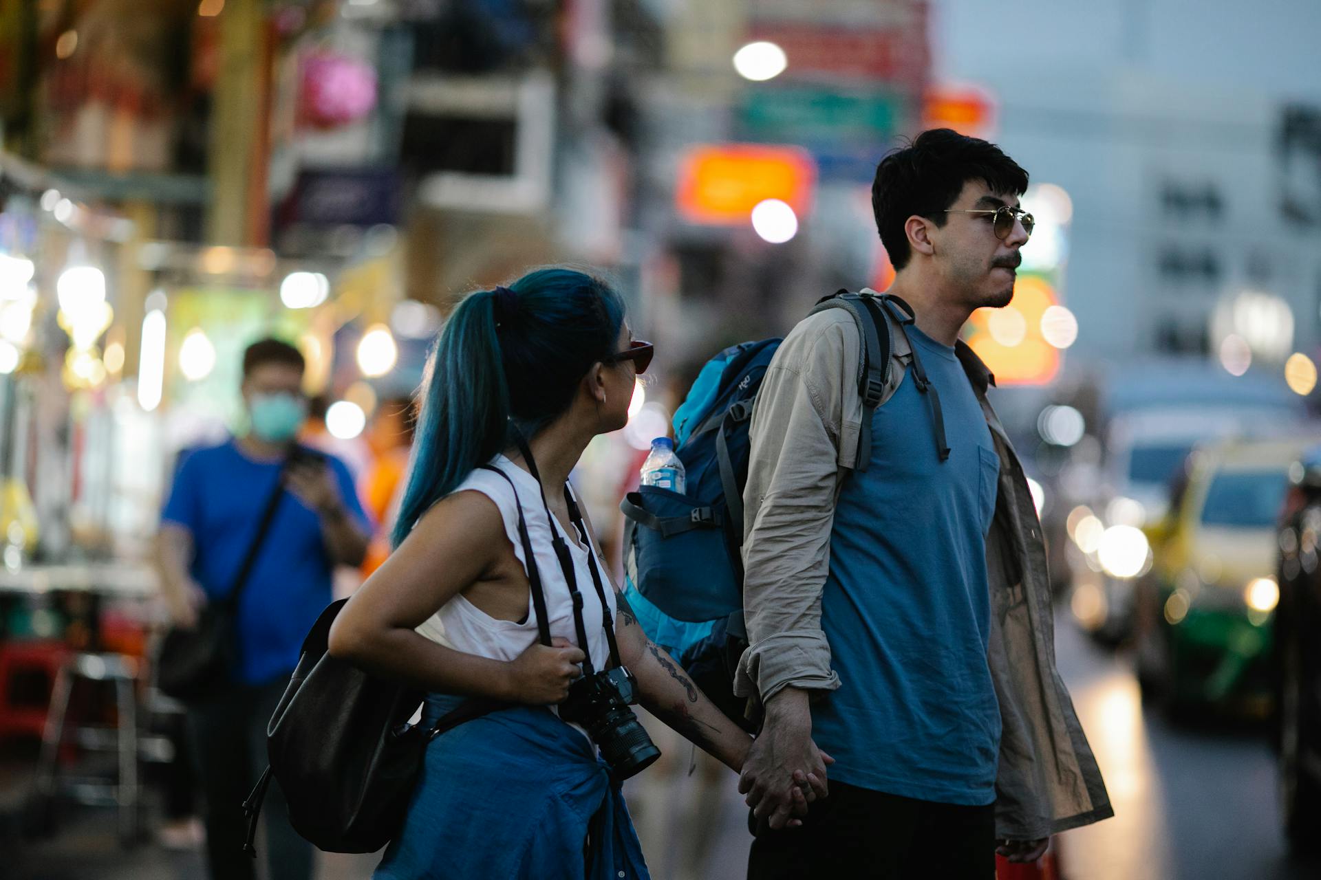 A young couple holding hands and exploring a vibrant night market, embodying adventure and travel.