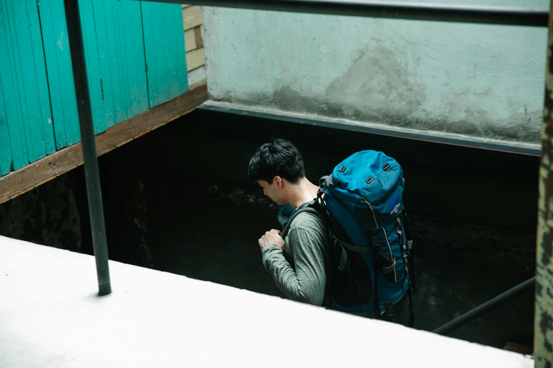 Man with backpack descends into an urban stairwell, exploring new environments.