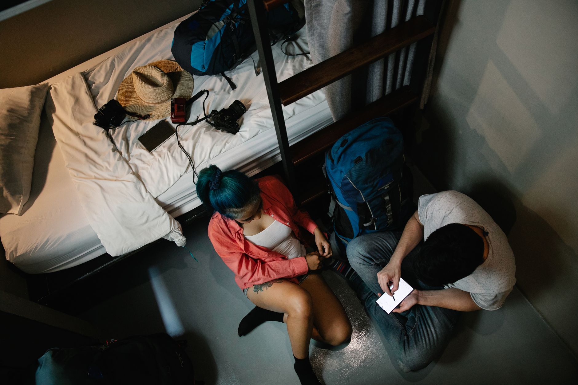 Best Cheap Phone for Travel: Protect Your Main Device A young couple using a smartphone in a hostel room with backpacks, ready for travel.