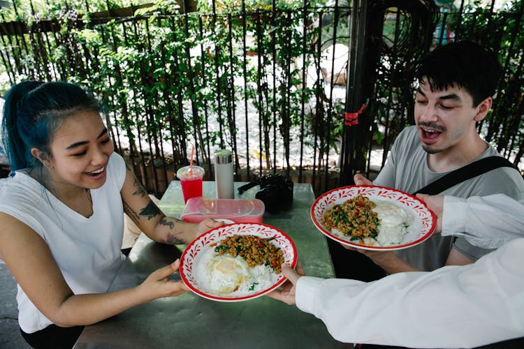 Waiter Serving A Fresh Meal To Young People In An Outdoor Restaurant 