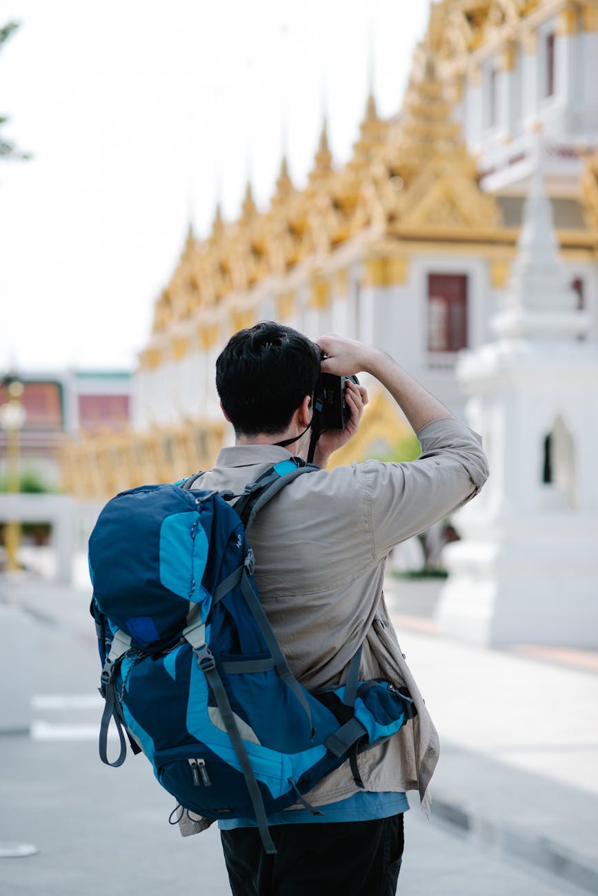A male tourist with a backpack photographing a temple, highlighting travel and exploration.