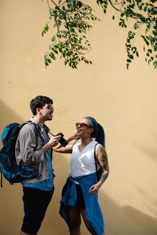 Free A cheerful moment of two tourists sharing a conversation against a sunny yellow wall. Stock Photo