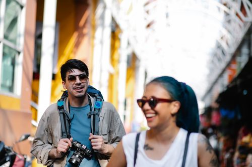 Free Joyful tourists walking through a colorful street market, capturing memories. Stock Photo