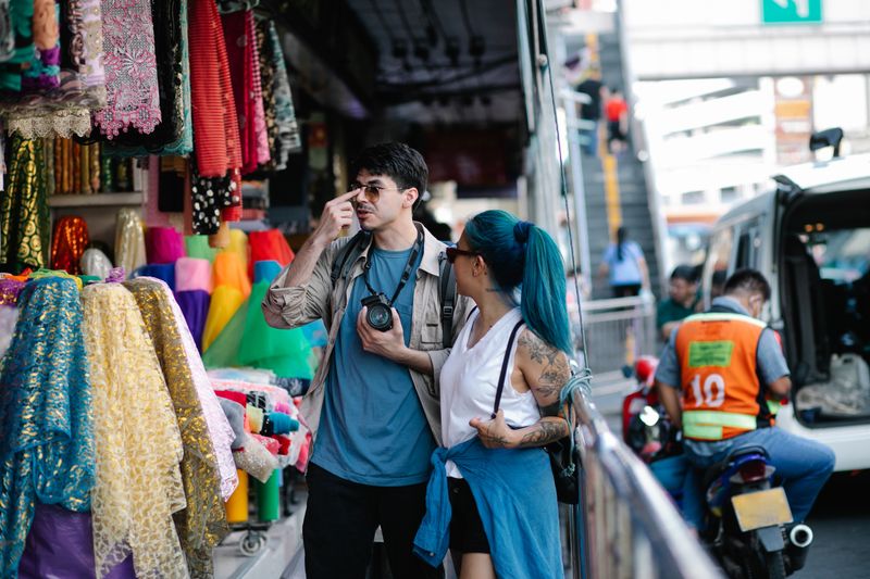 A couple enjoys a colorful street market with textiles and vendors nearby.