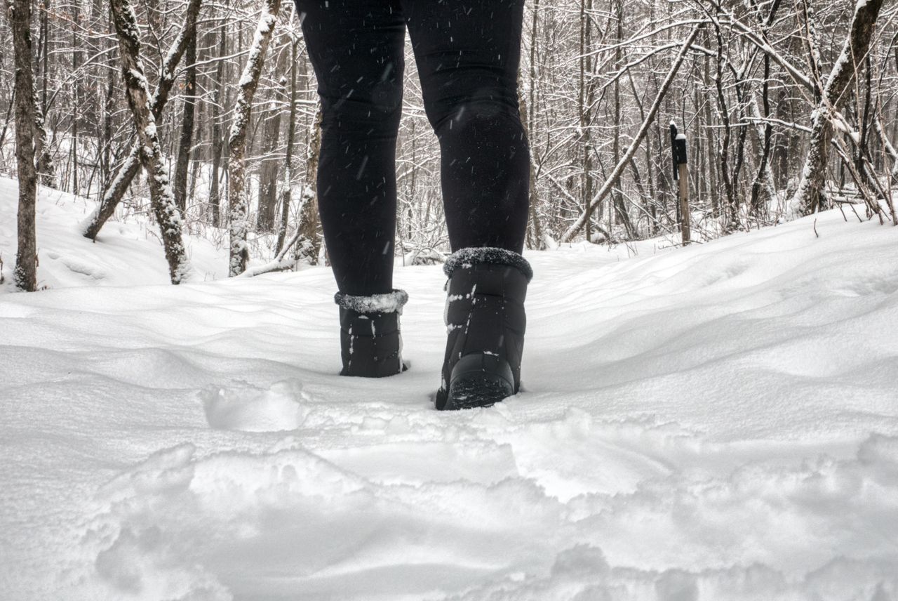 Person in fur-trimmed boots walking through a snowy forest