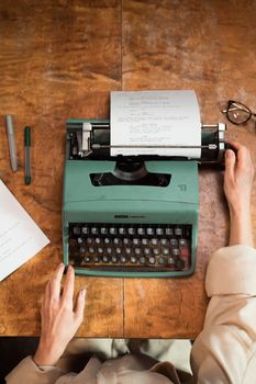 A overhead shot of hands typing on a vintage typewriter, set on a wooden desk.