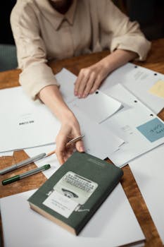 Close-up of individual organizing papers on a wooden table with pens and a book.