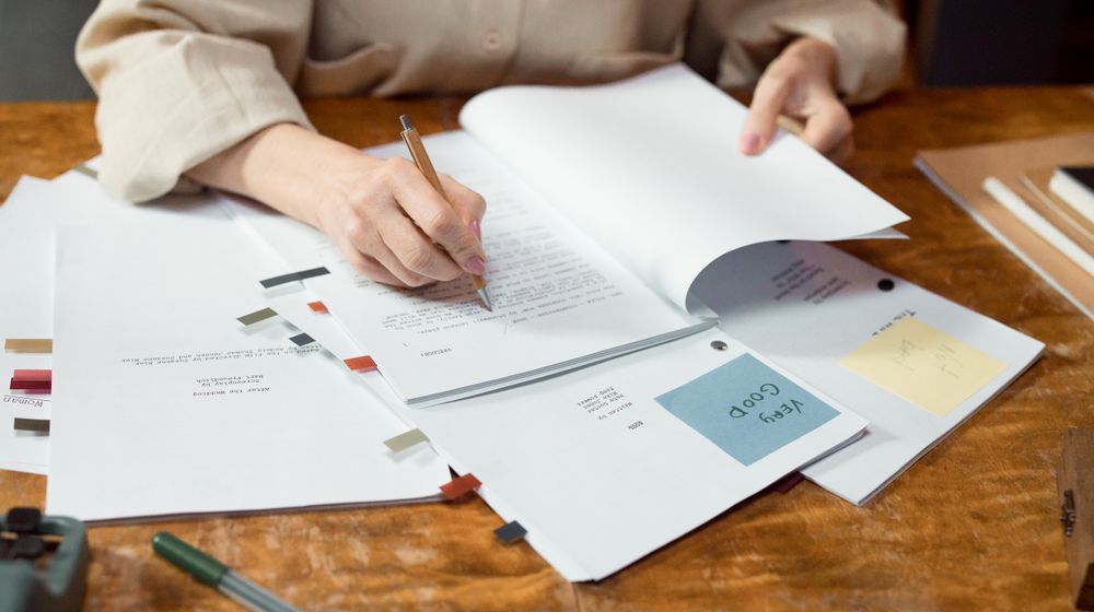 Close-up of hands writing and organizing documents on a wooden desk.