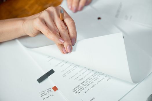 Close-up image of hands turning pages of a document on a desk indoors.