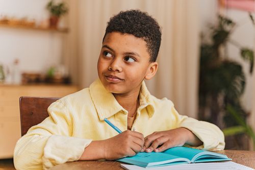 Free Young boy writing notes in a blue notebook indoors. Stock Photo