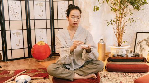 Asian woman meditating with a candle in a tranquil indoor setting, promoting relaxation and zen.