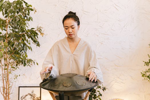 Asian woman plays hang drum indoors, creating a serene meditation ambience.