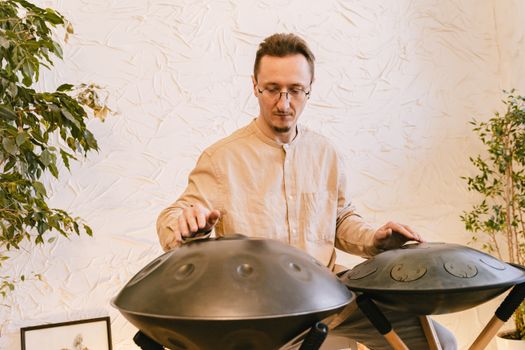 A man plays handpans indoors, creating a peaceful musical atmosphere.