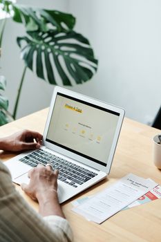 Adult using a laptop on a wooden desk with a large plant leaf in the background, creating a serene workspace.