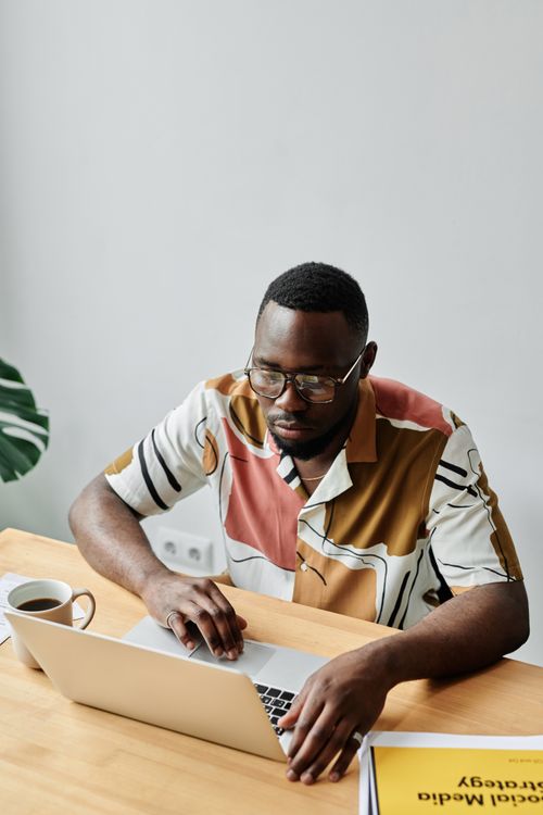 Free An adult man working on a laptop at a desk, wearing a patterned shirt and eyeglasses. Stock Photo