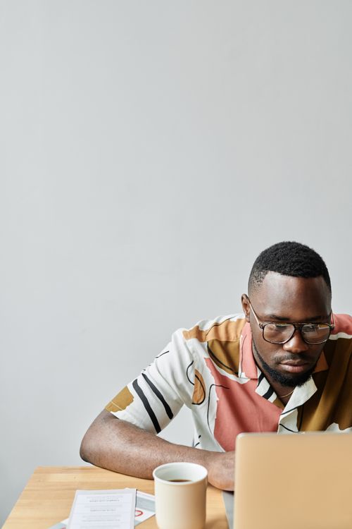 Free A man wearing eyeglasses works on his laptop indoors, concentrating on tasks. Stock Photo