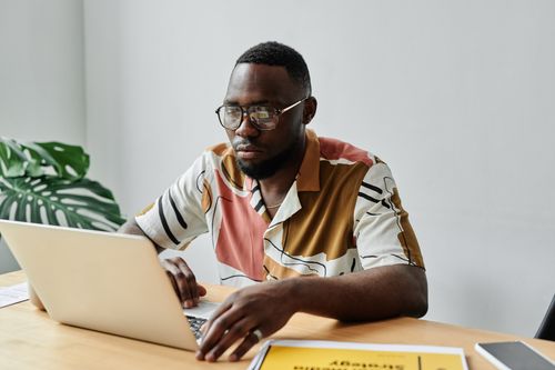 Free African American man using a laptop and working at a desk in an office setting. Stock Photo
