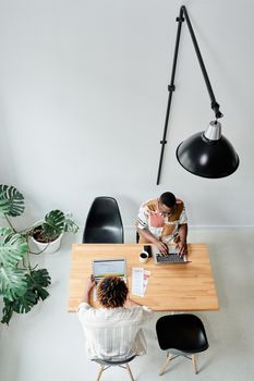 Top view of two adults working on laptops at a wooden table in a modern office setting.