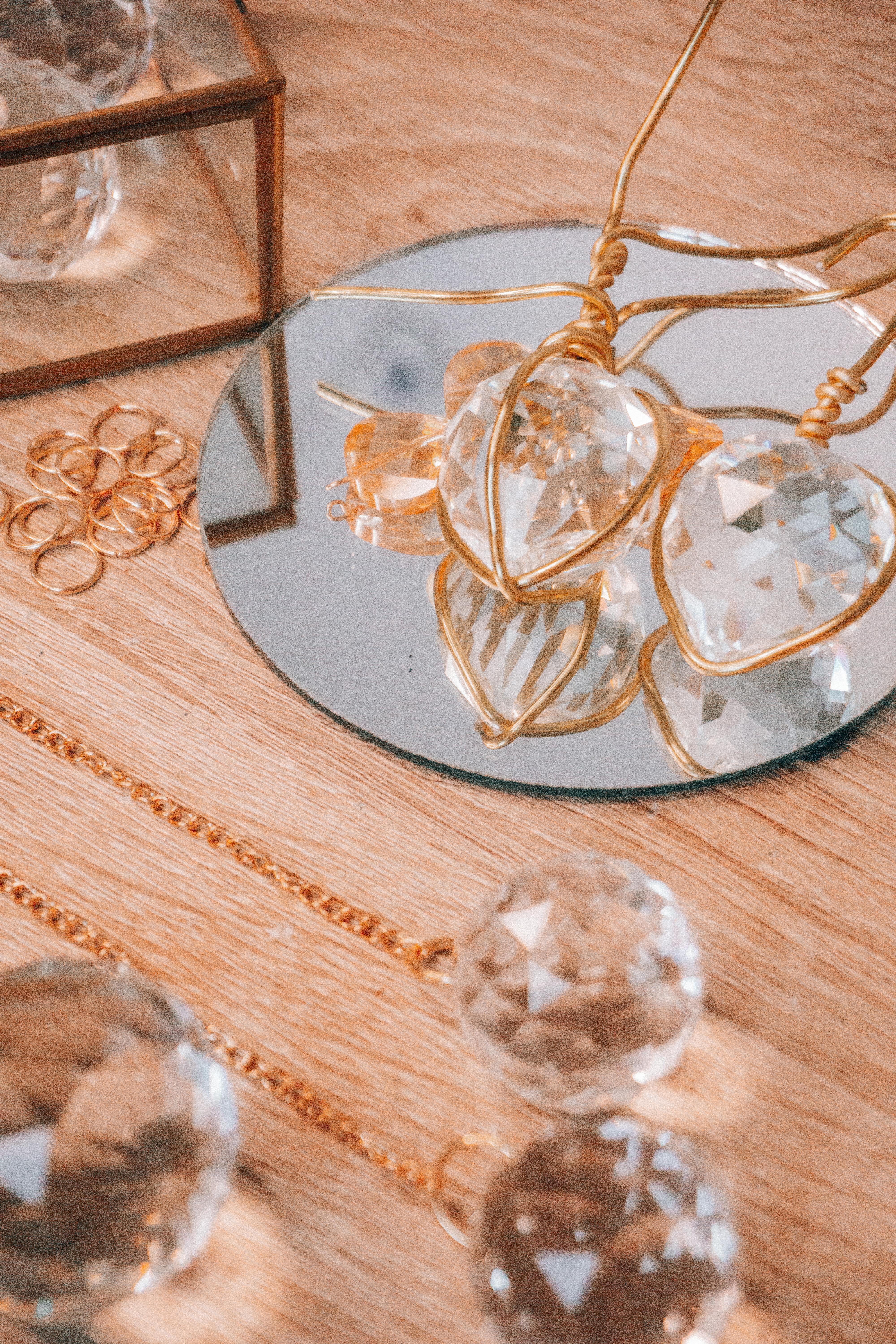 Elegant arrangement of crystal ornaments and gold jewelry on a mirror reflecting light.