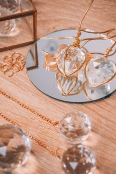 Elegant arrangement of crystal ornaments and gold jewelry on a mirror reflecting light.