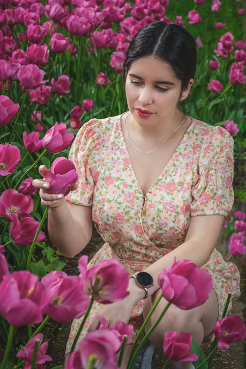 Close-Up Photo of a Beautiful Woman in a Floral Dress Touching Pink Tulips