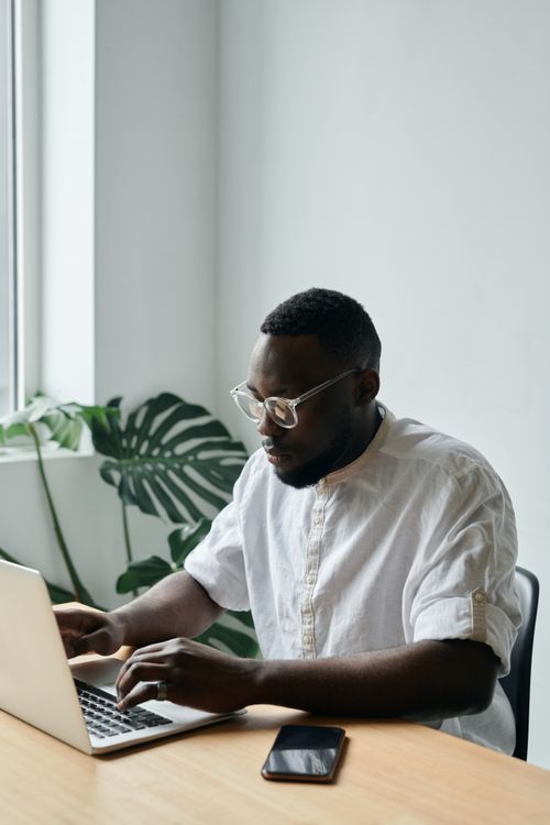 Free African American man typing on a laptop at a desk in a modern office. Stock Photo