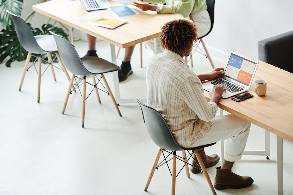 Free Man In Striped Long Sleeve Shirt Sitting On Table Using Laptop Stock Photo