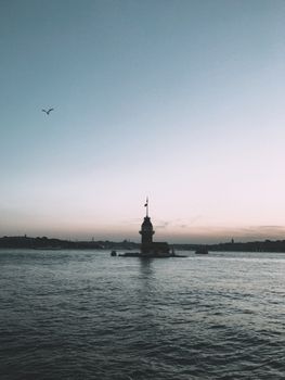 Lighthouse tower located in middle of clear sea under cloudless sky at sunset