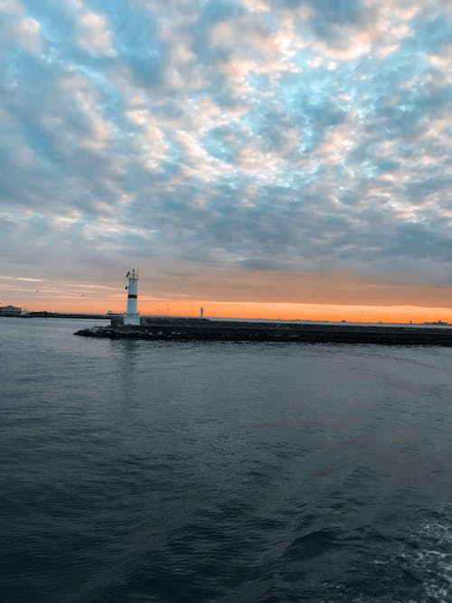 Pier with lighthouse near sea at sunset