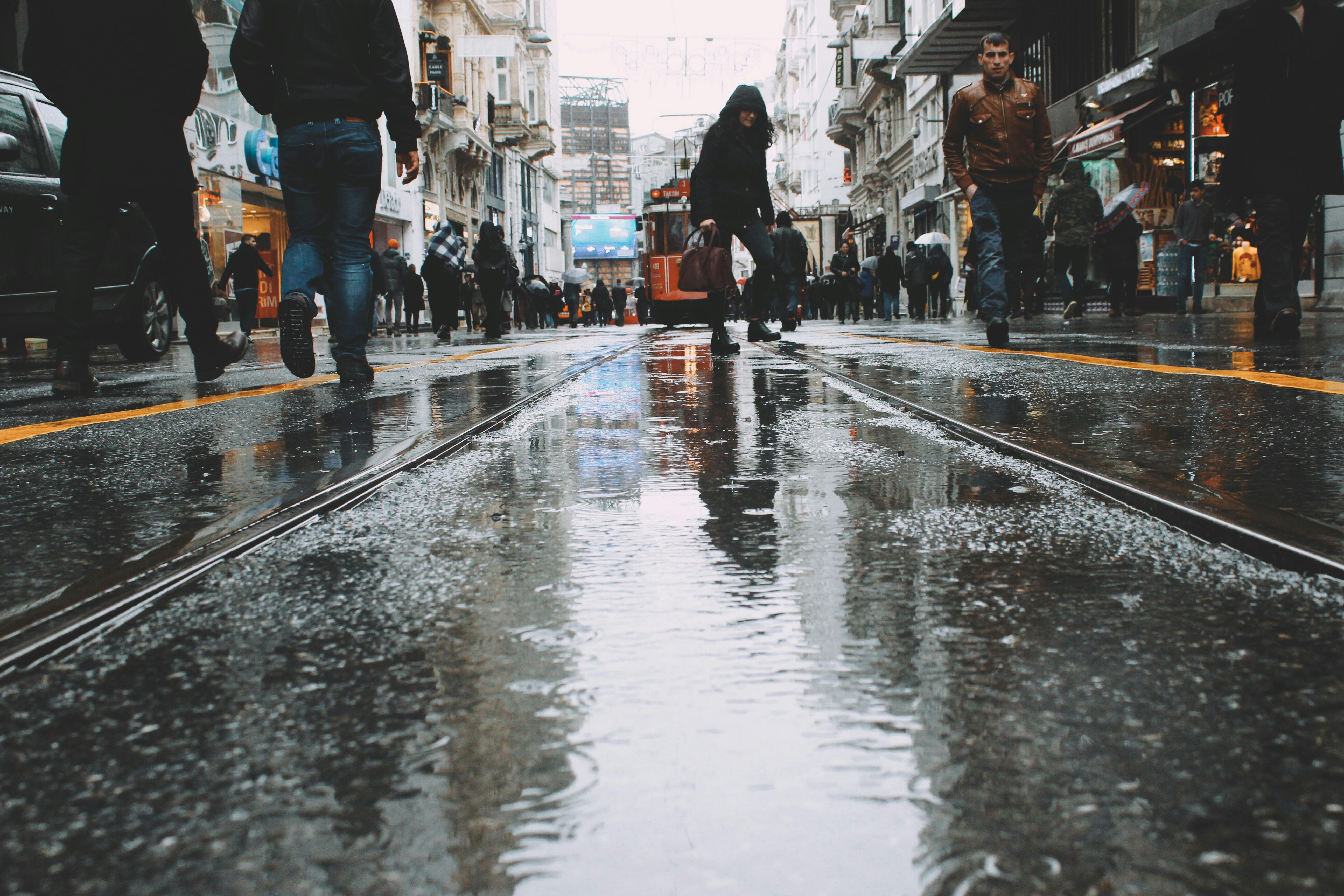 Crowd of people walking on wet asphalt road with tram rails between old buildings and local shops in overcast day by Leo Arslan