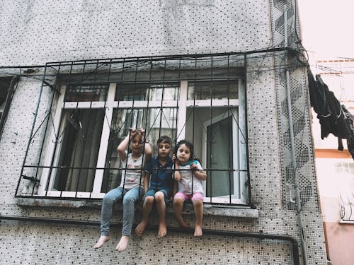 Free Barefoot ethnic kids sitting on window grate Stock Photo