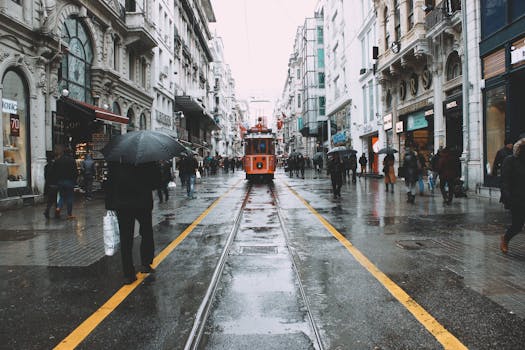 Tram riding on rails on wet street between pedestrians walking with umbrellas in historic district in rainy day