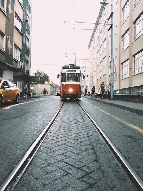 Vintage tram with glowing headlight riding on rails past pedestrians and residential buildings