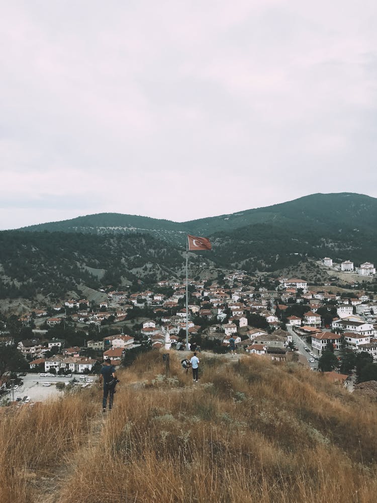 People Standing On Hill With Waving Flag And Observing Cityscape