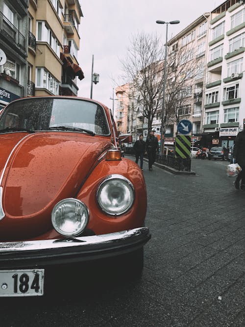 Glossy red old fashioned car covered with drops of water parked on street near residential building