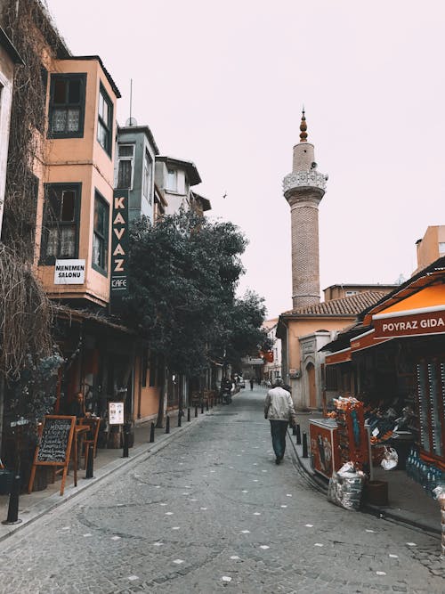 Male strolling on narrow paved alley with typical residential building outdoor cafes and minaret of mosque in Turkey