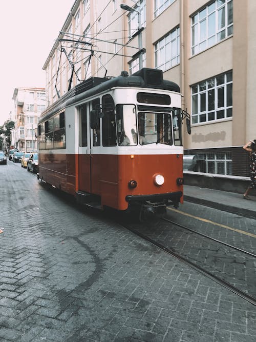 Vintage tramway and cars driving on paved road near residential buildings in city