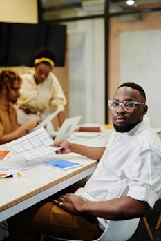 Professional African American man in glasses working with colleagues in a modern office environment.