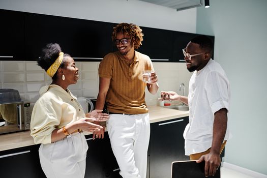 A joyful group of colleagues in an office kitchen, laughing and conversing during a break.