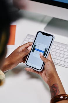 A close-up view of a person using a smartphone in front of a computer keyboard at a desk.