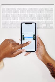 Hands using a smartphone in front of a white keyboard, focusing on touchscreen interaction.